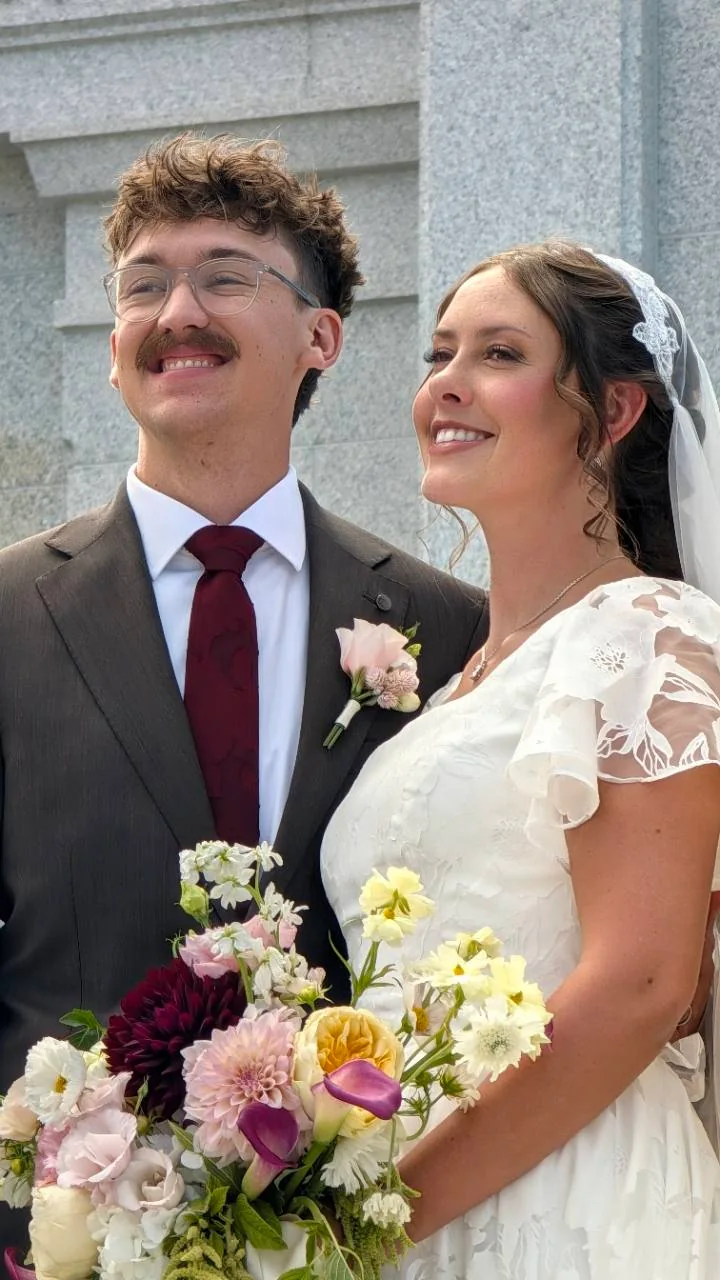 Sage and Quentin smiling together in their wedding clothes, with Sage holding her bouquet.